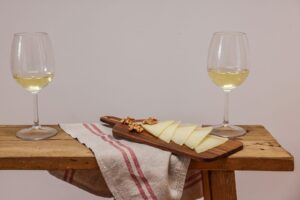 Zwei Gläser Weißwein neben Käse und Walnüssen auf einem Brett