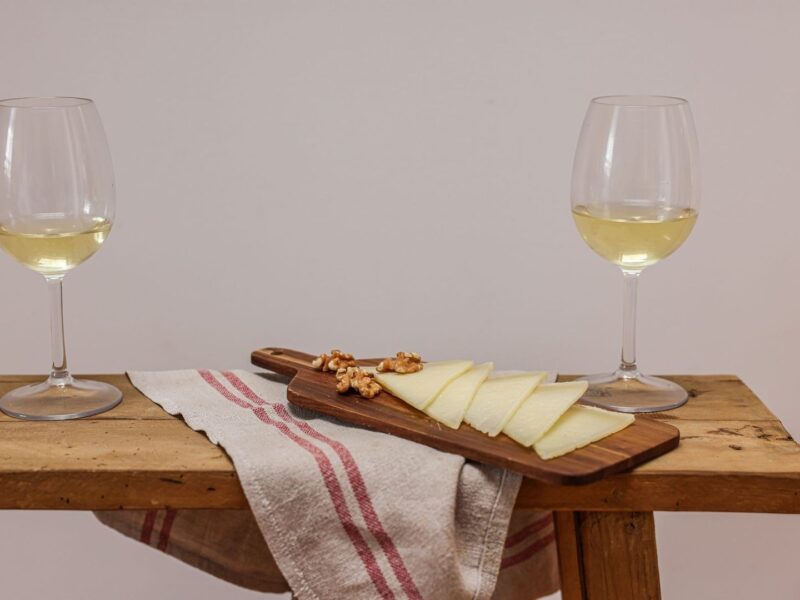Zwei Gläser Weißwein neben Käse und Walnüssen auf einem Brett