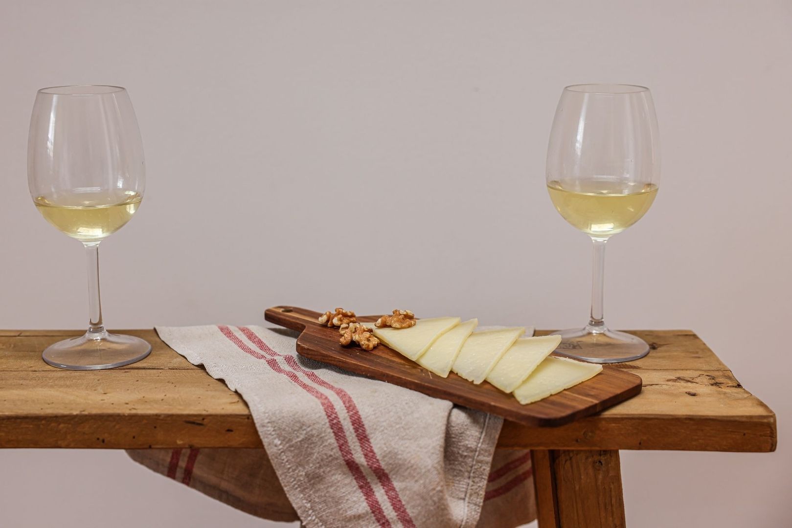 Zwei Gläser Weißwein neben Käse und Walnüssen auf einem Brett